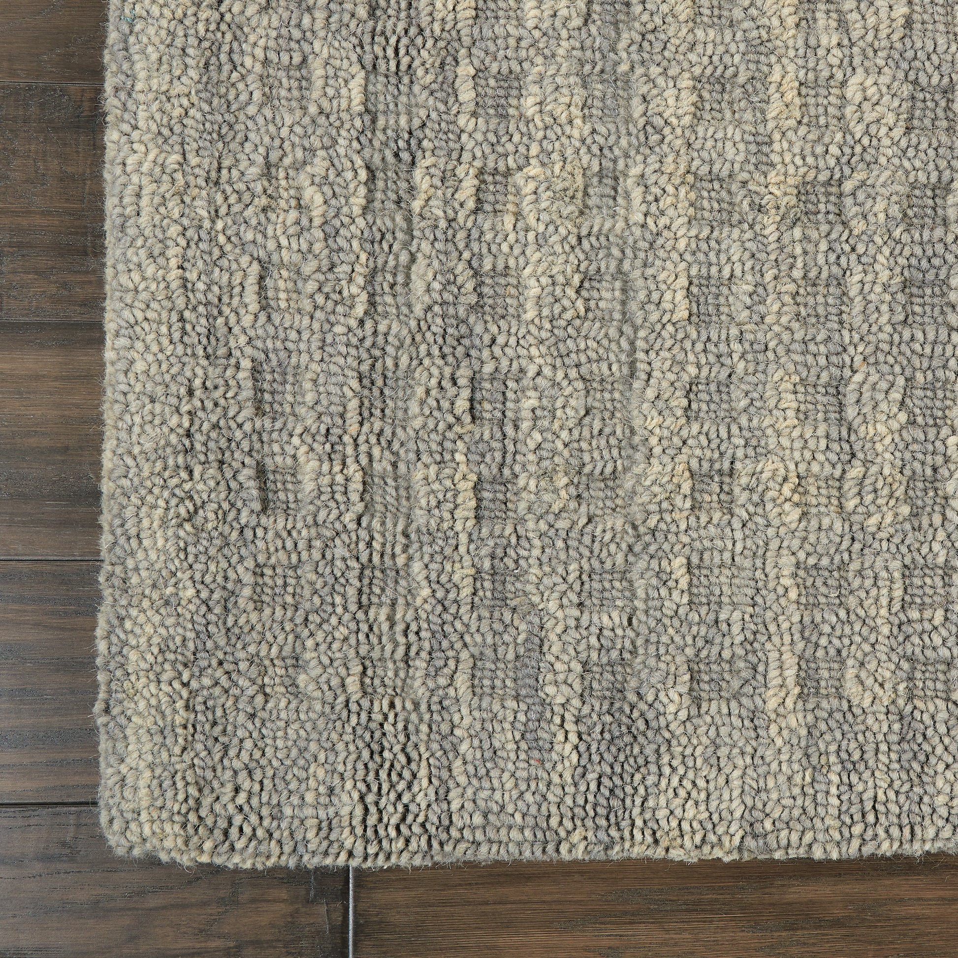 Gray and beige boucle rug with thick textured loops on dark wood floor; rectangular edge visible.