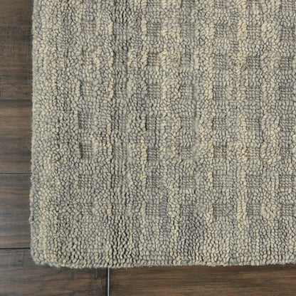 Gray and beige boucle rug with thick textured loops on dark wood floor; rectangular edge visible.