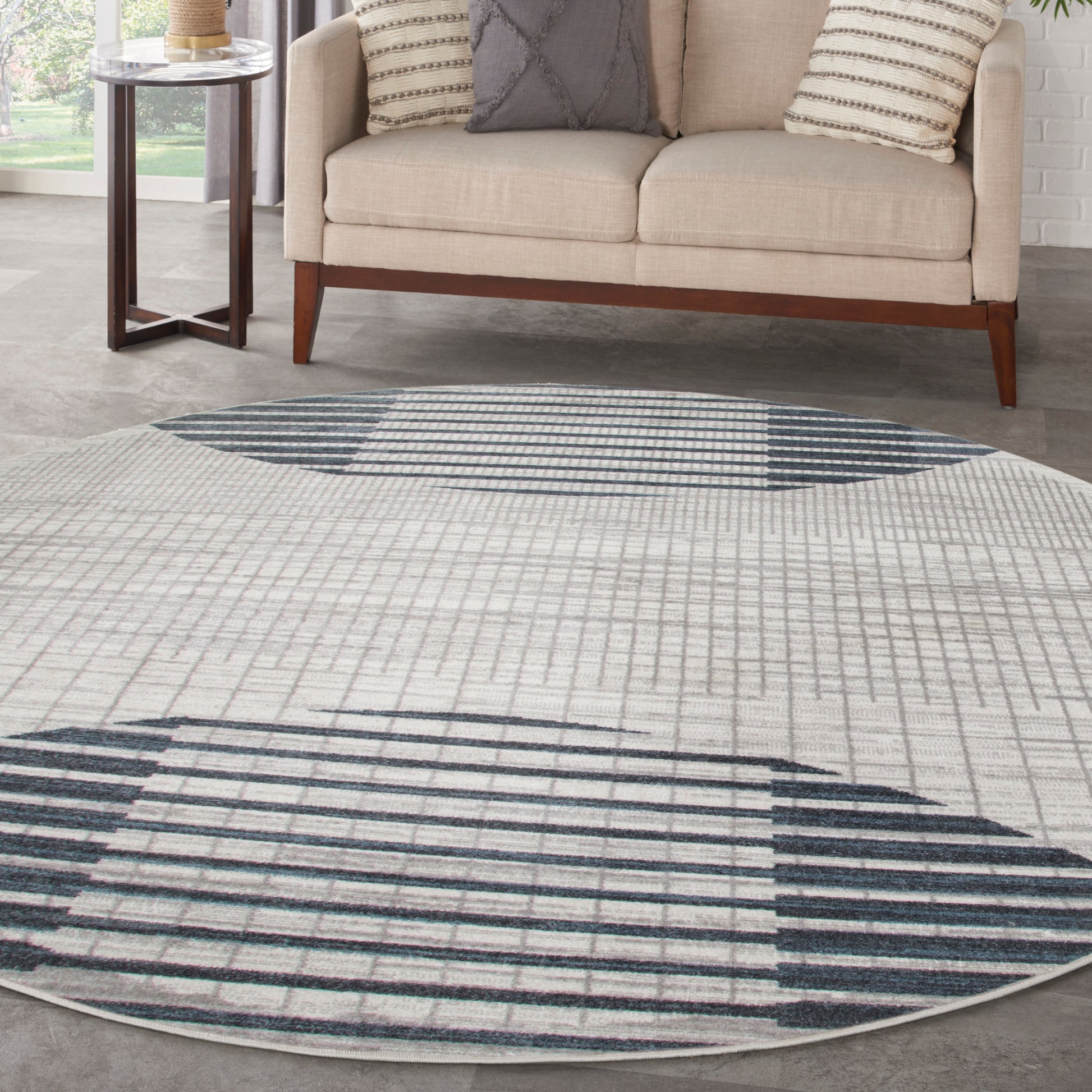 Round cream rug with navy geometric lines, in a living room with a beige sofa, dark wood legs, and a side table.