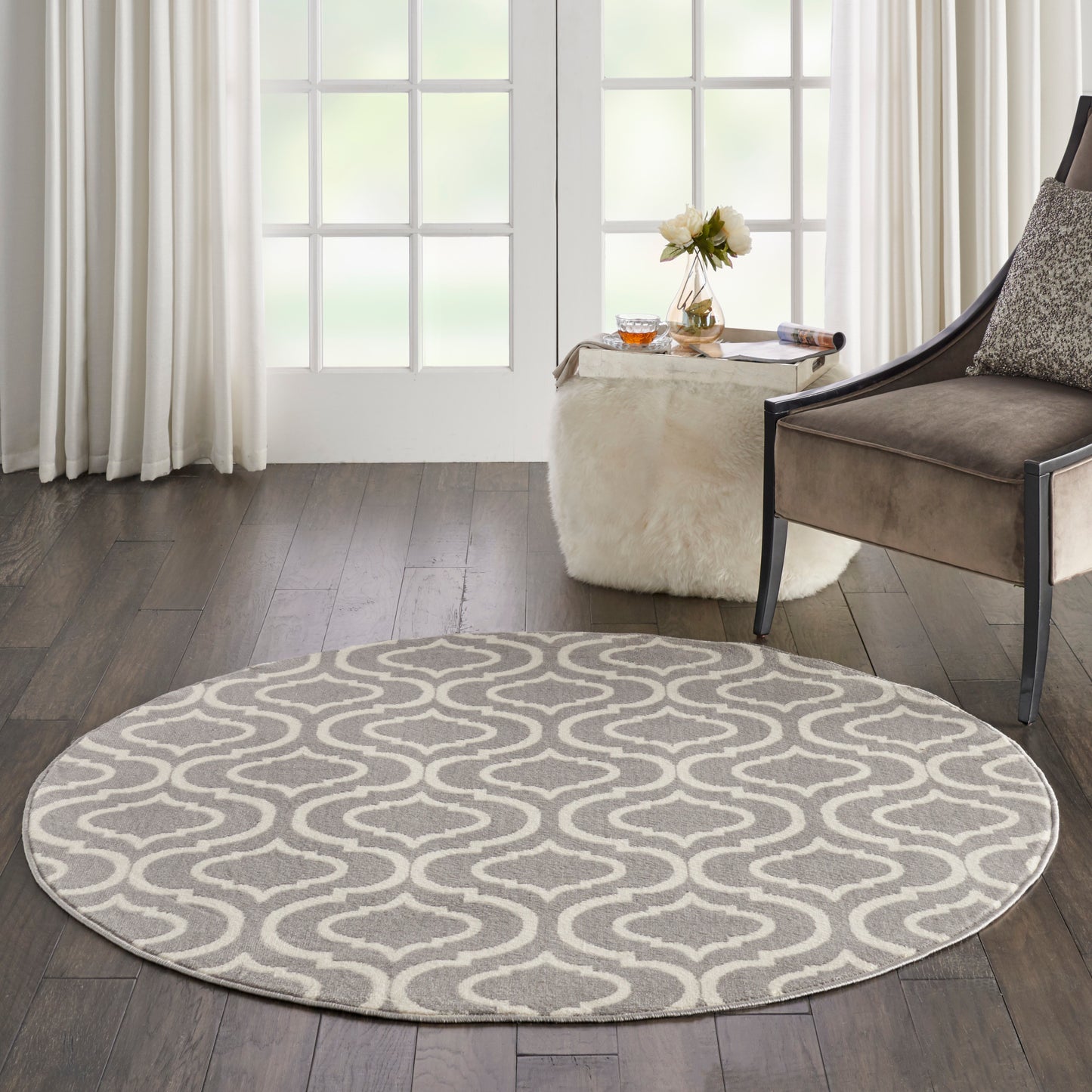 Round grey and white rug with a wavy geometric pattern in a modern living room beside a brown upholstered chair.