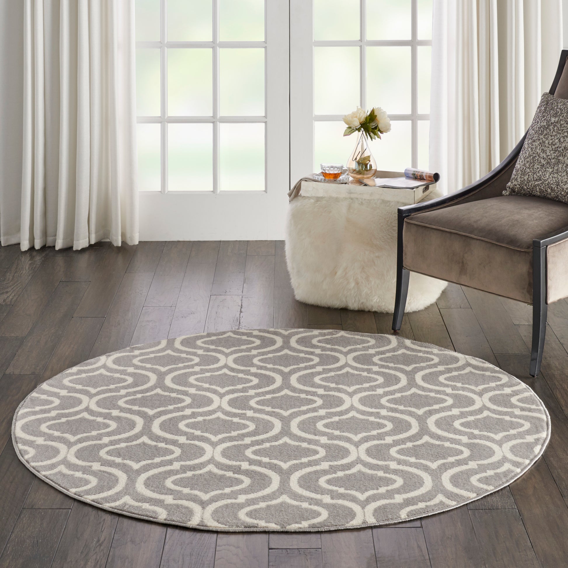 Round grey and white rug with a wavy geometric pattern in a modern living room beside a brown upholstered chair.