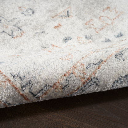Light-gray plush rug with blue and orange geometric accents, folded edge visible on dark hardwood floor.