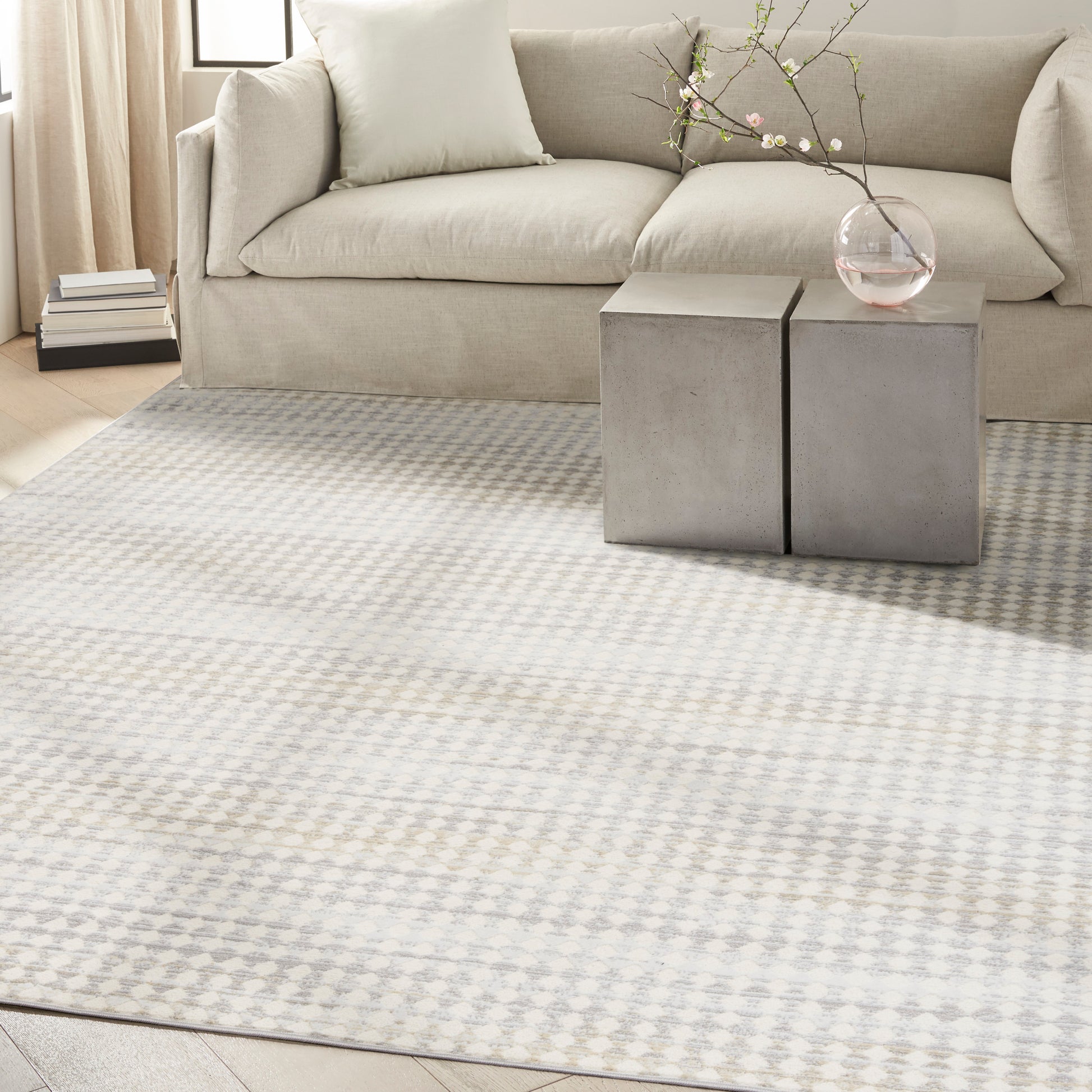 Light gray geometric patterned area rug under a beige fabric sofa with concrete cube side tables and a glass vase.