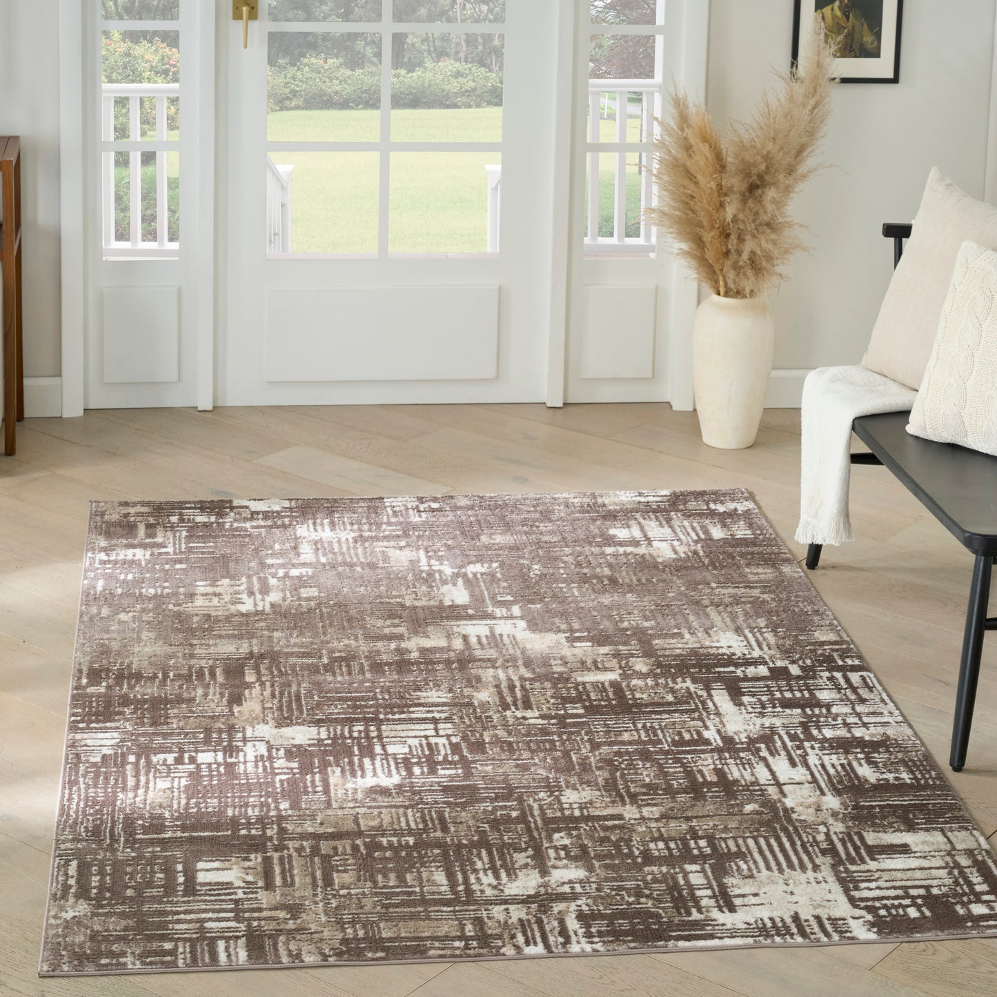 Abstract brown and cream area rug on light wood floor in a bright living room with white-framed doors and beige sofa.