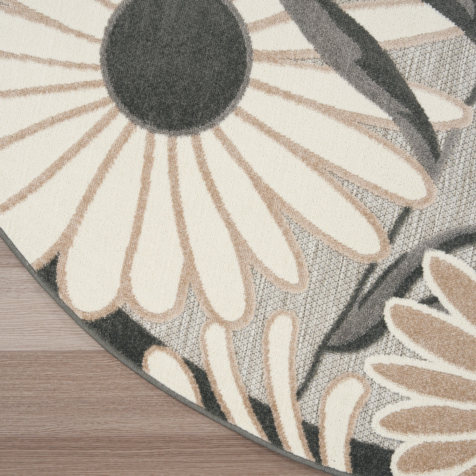 Floral round rug with beige daisy petals and dark centers on a gray background; soft textile on a wooden floor.