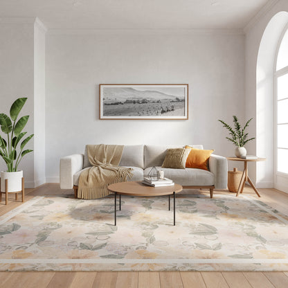 Bright living room with light gray sofa, beige throw, orange pillow, round wood coffee table, pastel floral rug, plants.