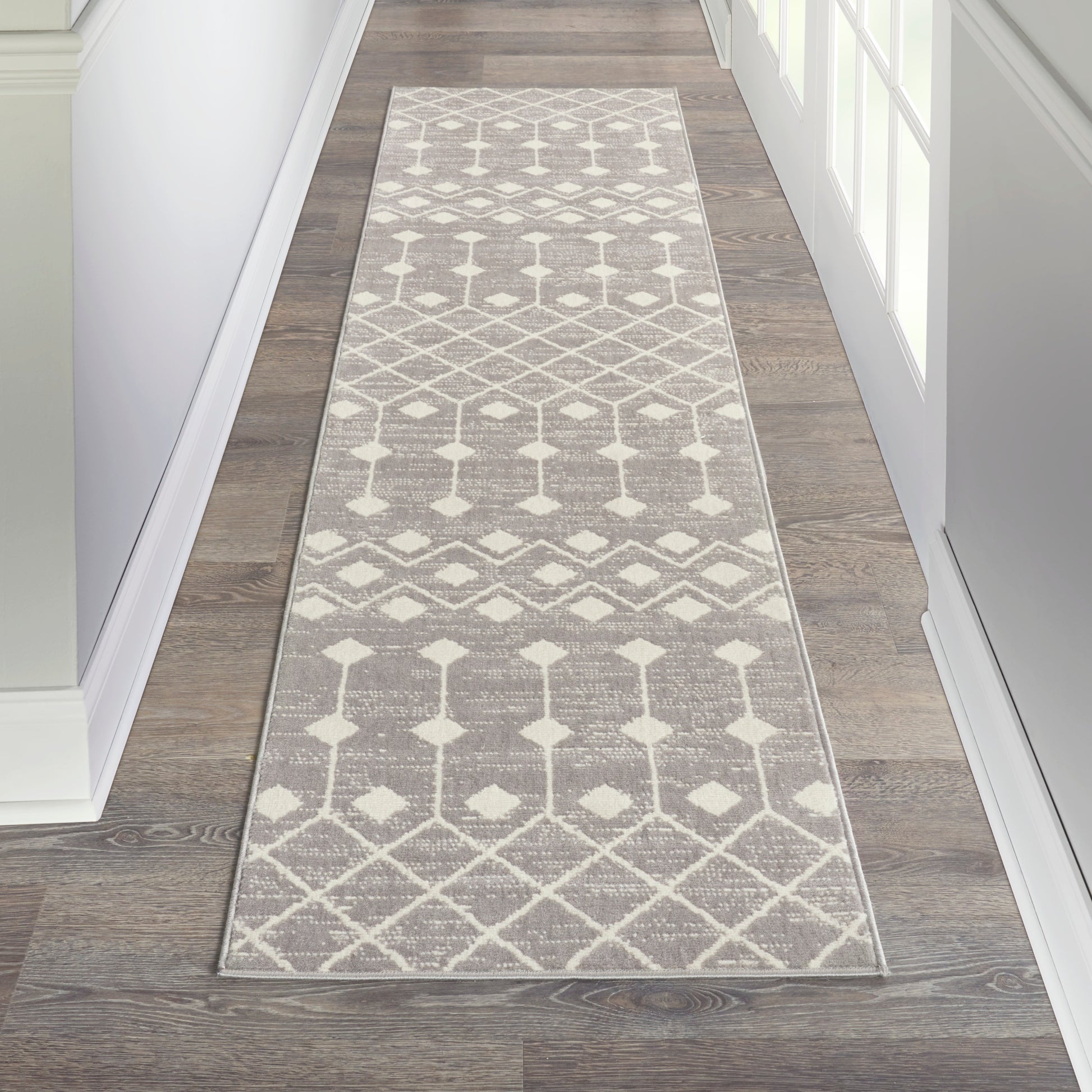 Rectangular gray and white geometric runner rug with diamond lattice pattern in a hardwood hallway.