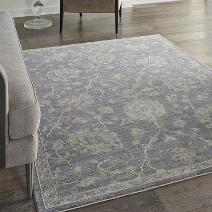 Rectangular blue-gray rug with ivory floral pattern and light border, soft pile beside a light gray sofa.