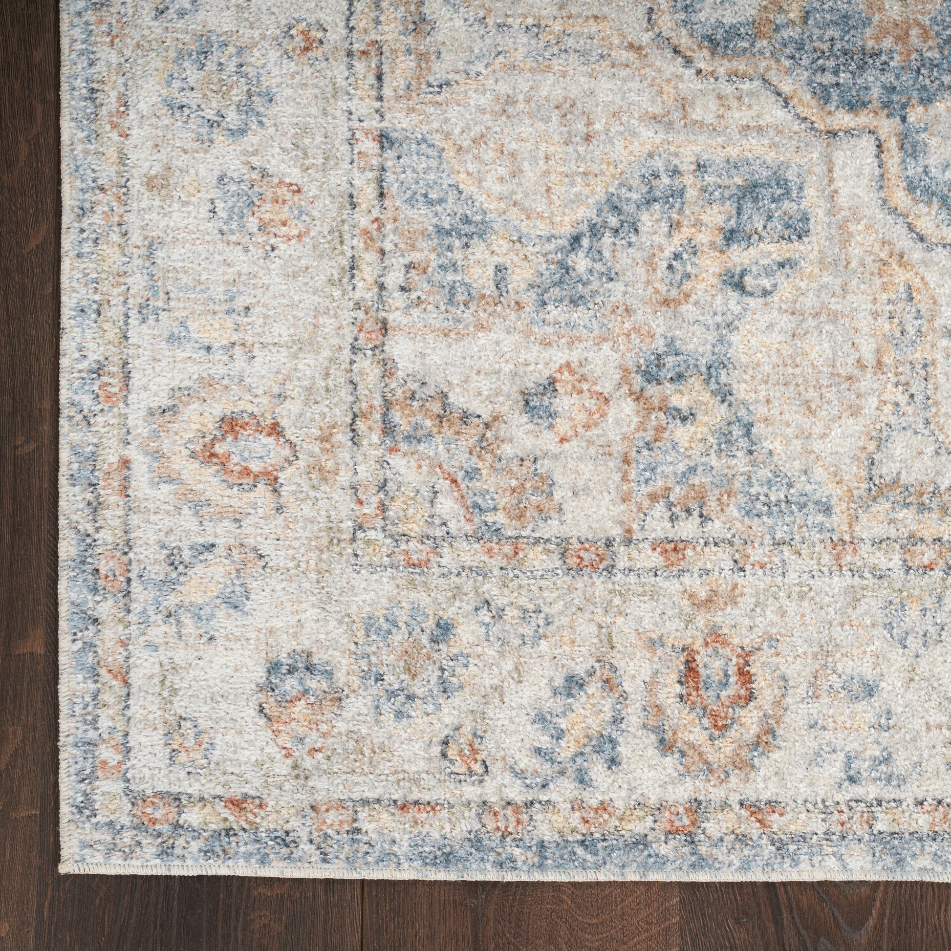 Rectangular distressed oriental rug in ivory, light blue, tan and rust on dark hardwood floor.