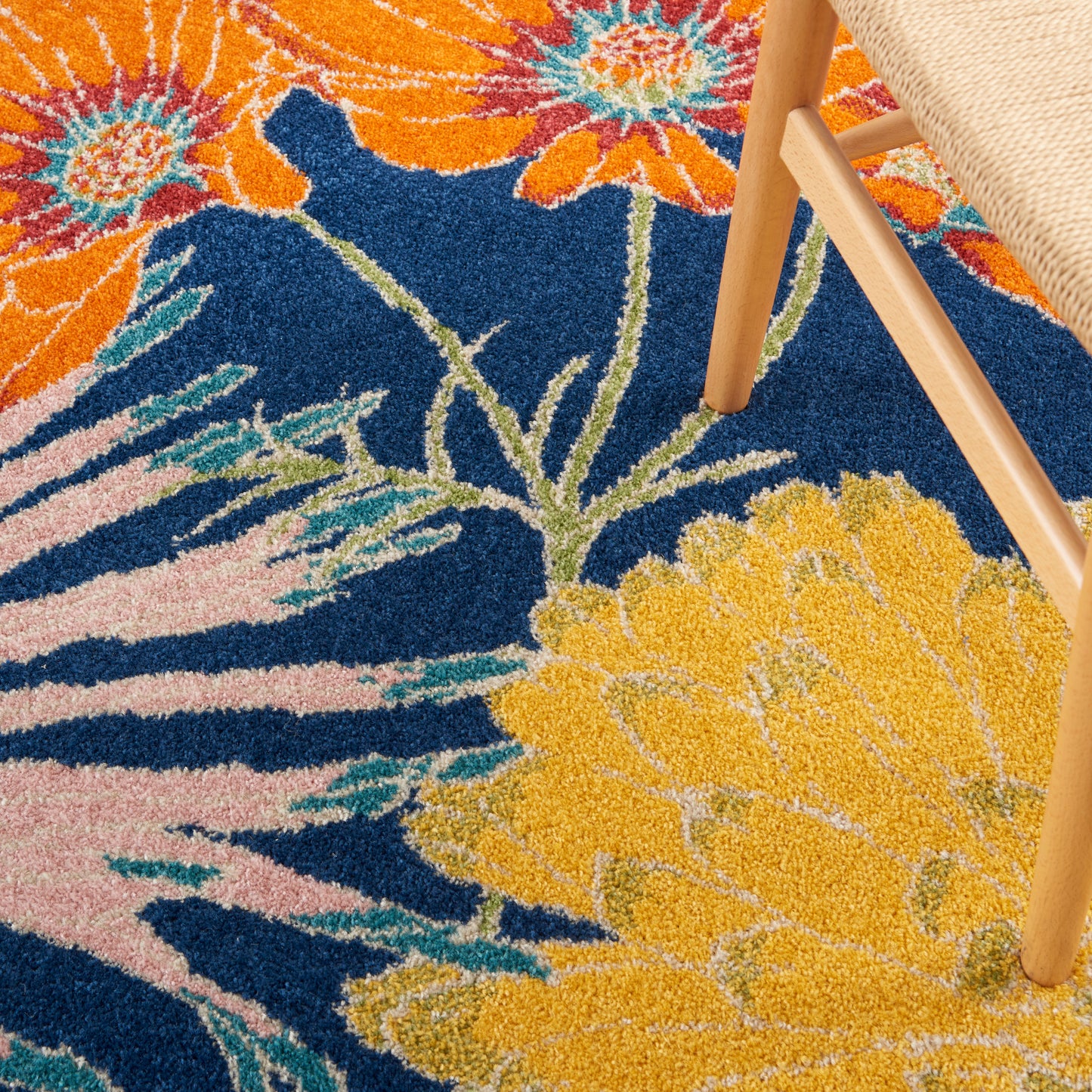 Vibrant floral shag rug with large orange, yellow and pink blossoms on a dark blue background; wooden chair leg rests on pile.