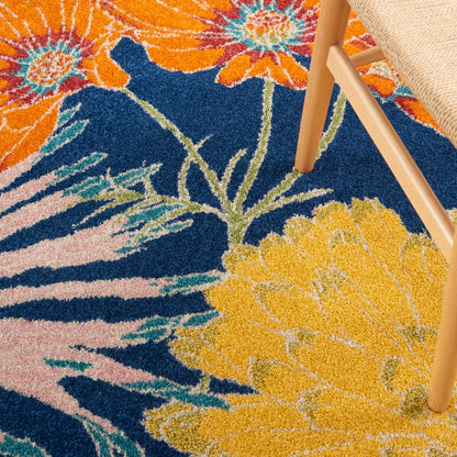 Vibrant floral shag rug with large orange, yellow and pink blossoms on a dark blue background; wooden chair leg rests on pile.