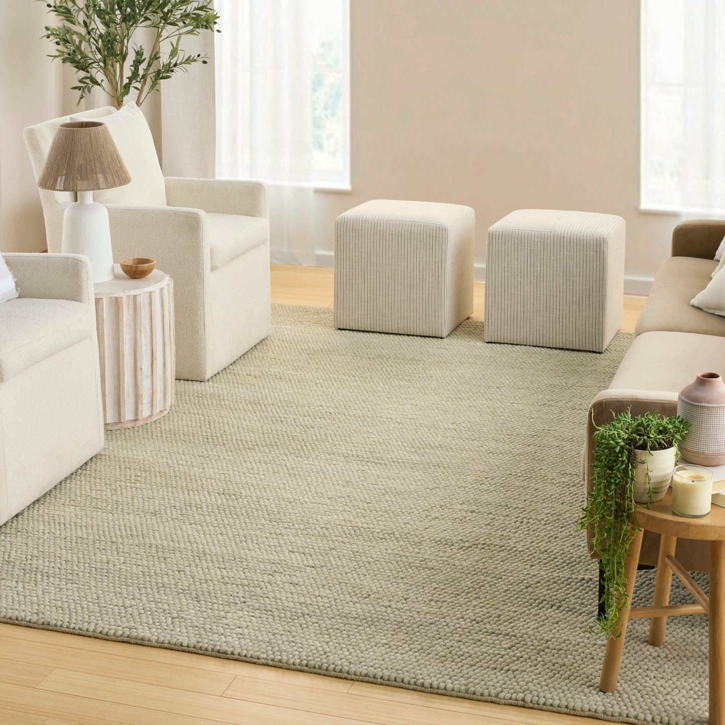 Neutral living room with cream sofas, beige woven rug, two light-grey ottomans, and wooden accent tables.