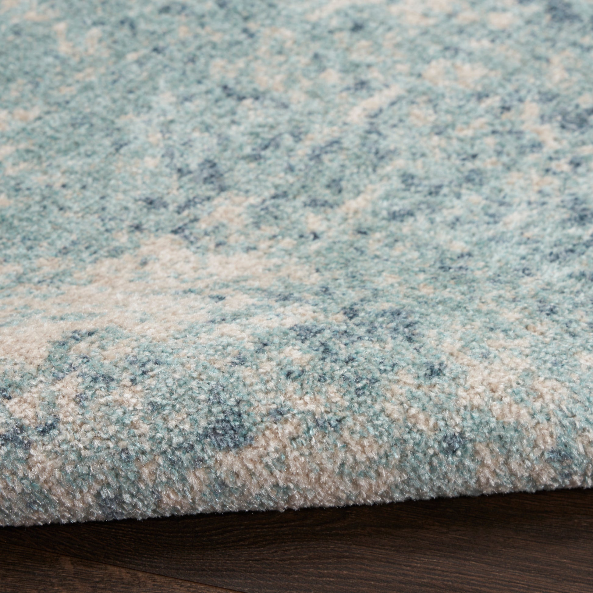 Blue and beige patterned rug with soft plush pile; edge folded over dark wood floor.