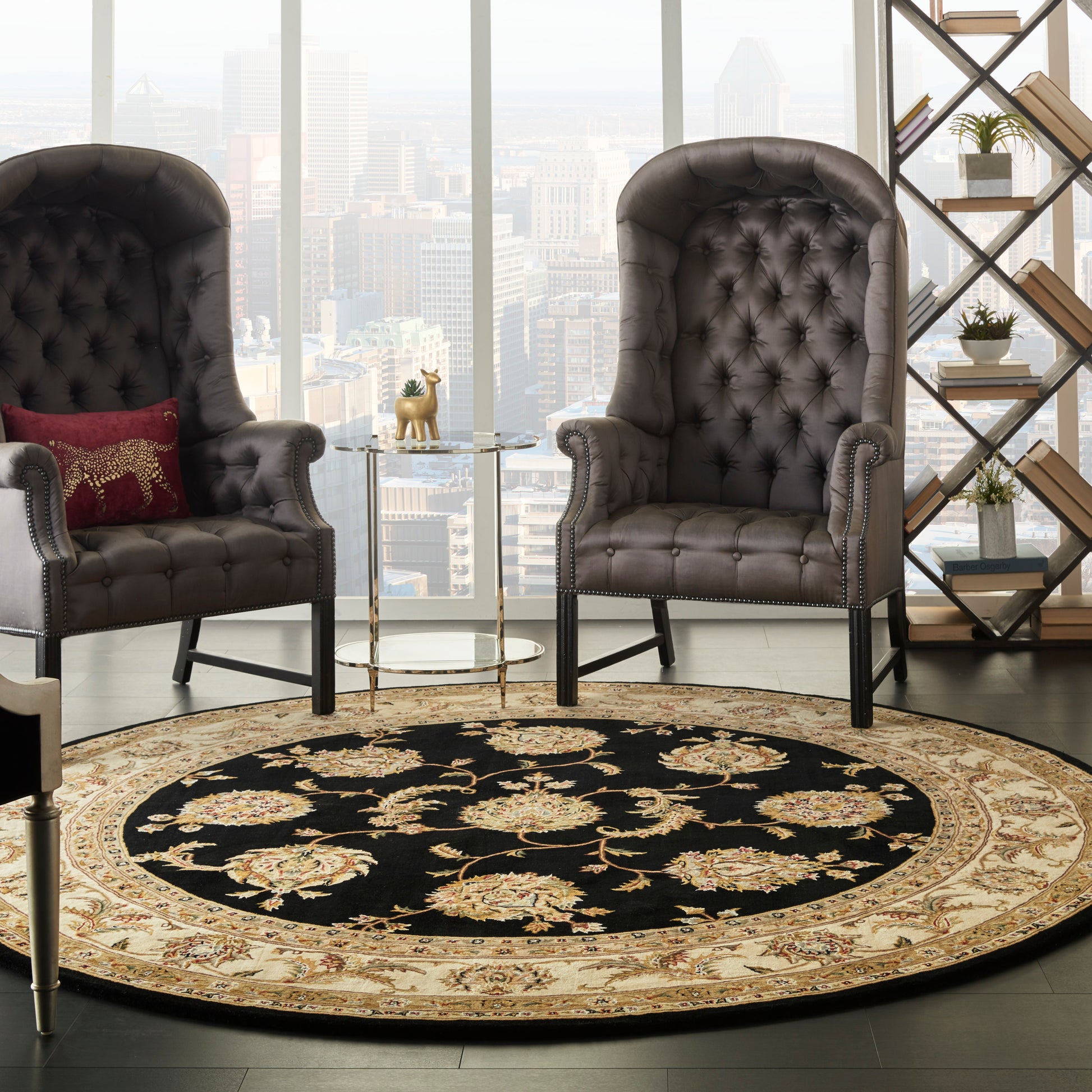Two dark brown tufted leather armchairs with nailhead trim around a round oriental rug with black center and gold border.