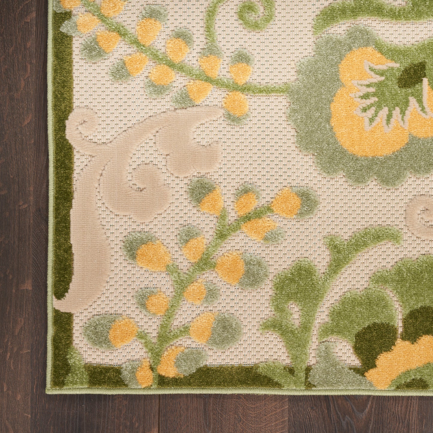 Beige textured rug with olive-green border and yellow-green botanical pattern, on dark wood floor.