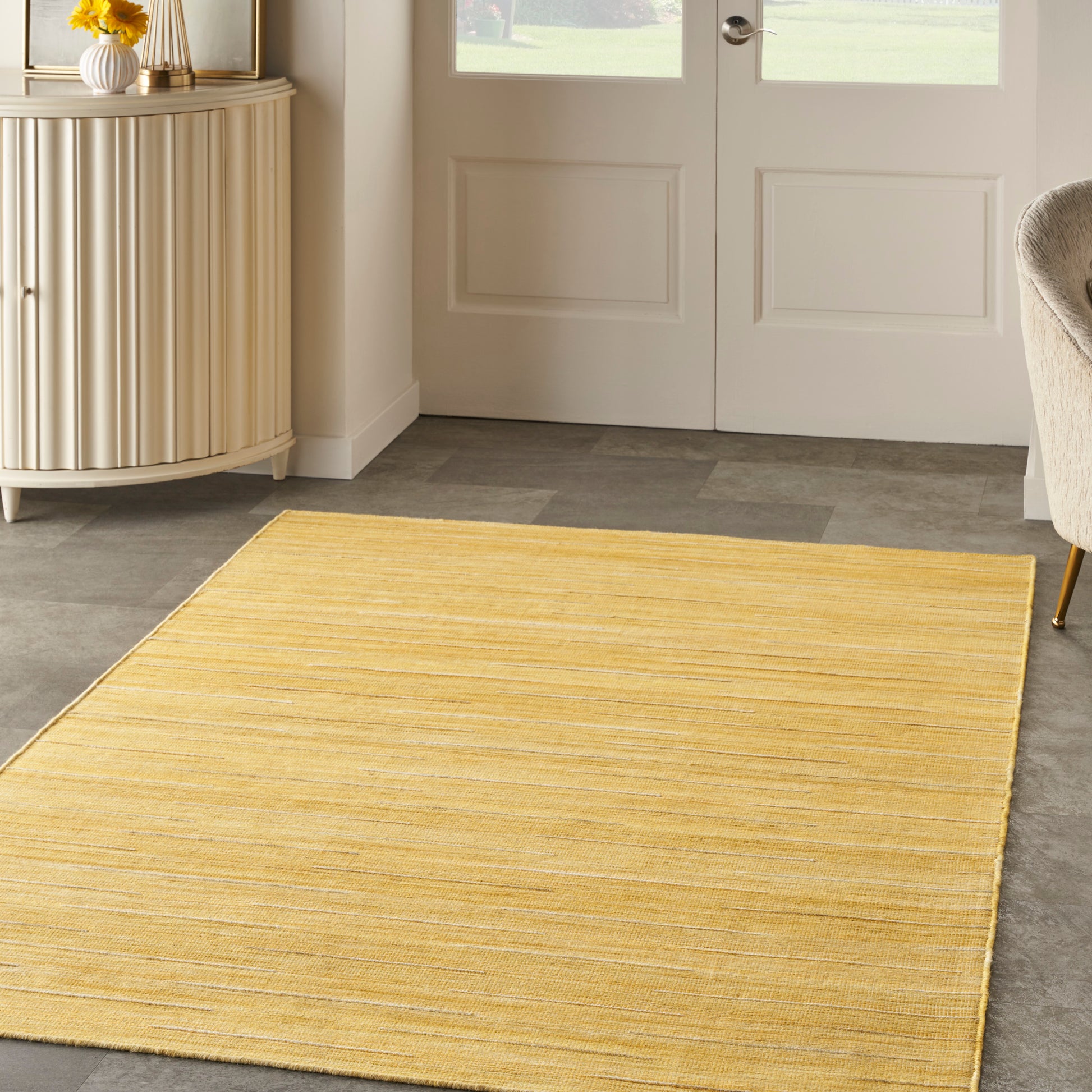 Mustard yellow woven area rug in a bright entryway with a light cabinet and glass-paneled doors.