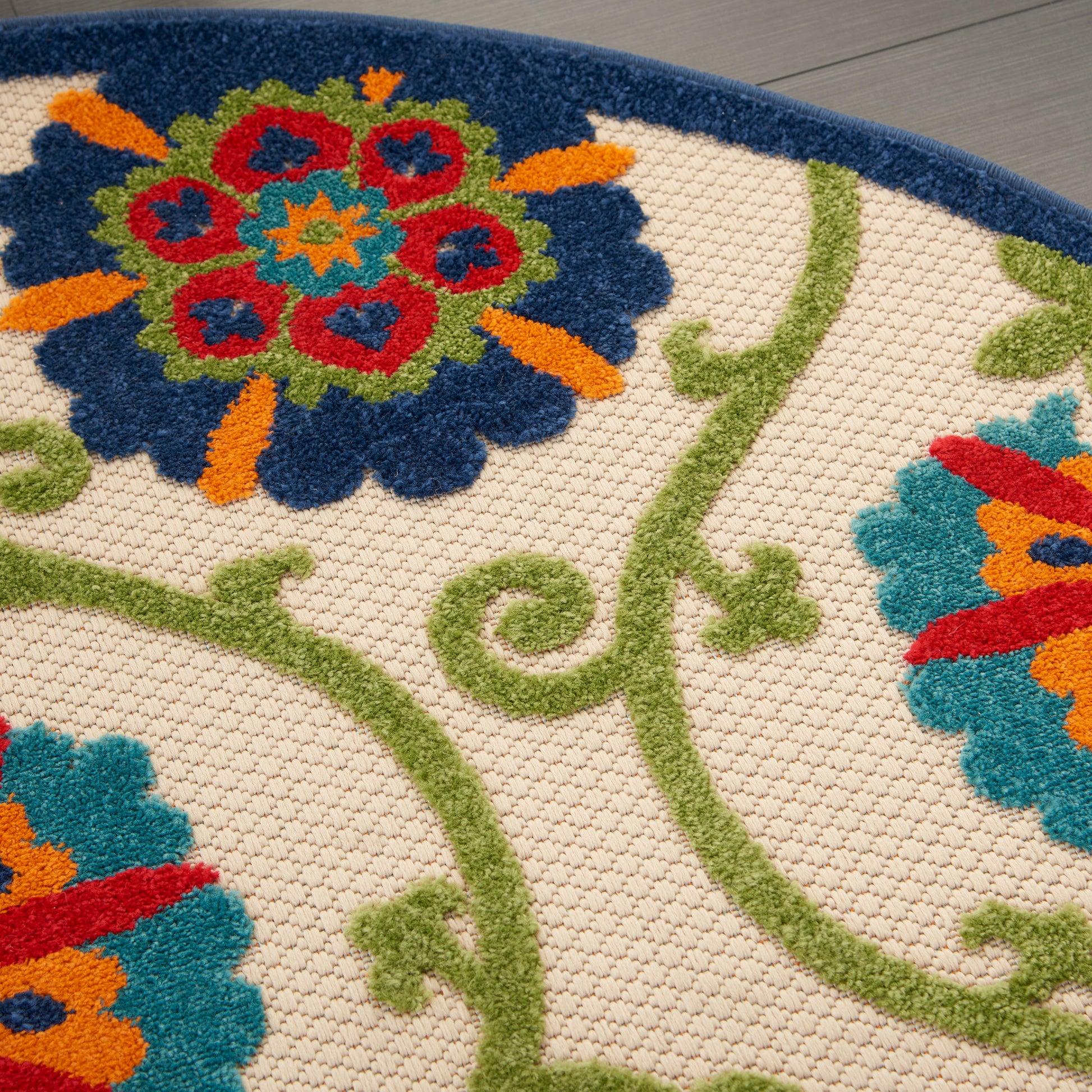 Close-up of a beige textured rug with green vines and vibrant blue, red, orange, teal floral motifs.