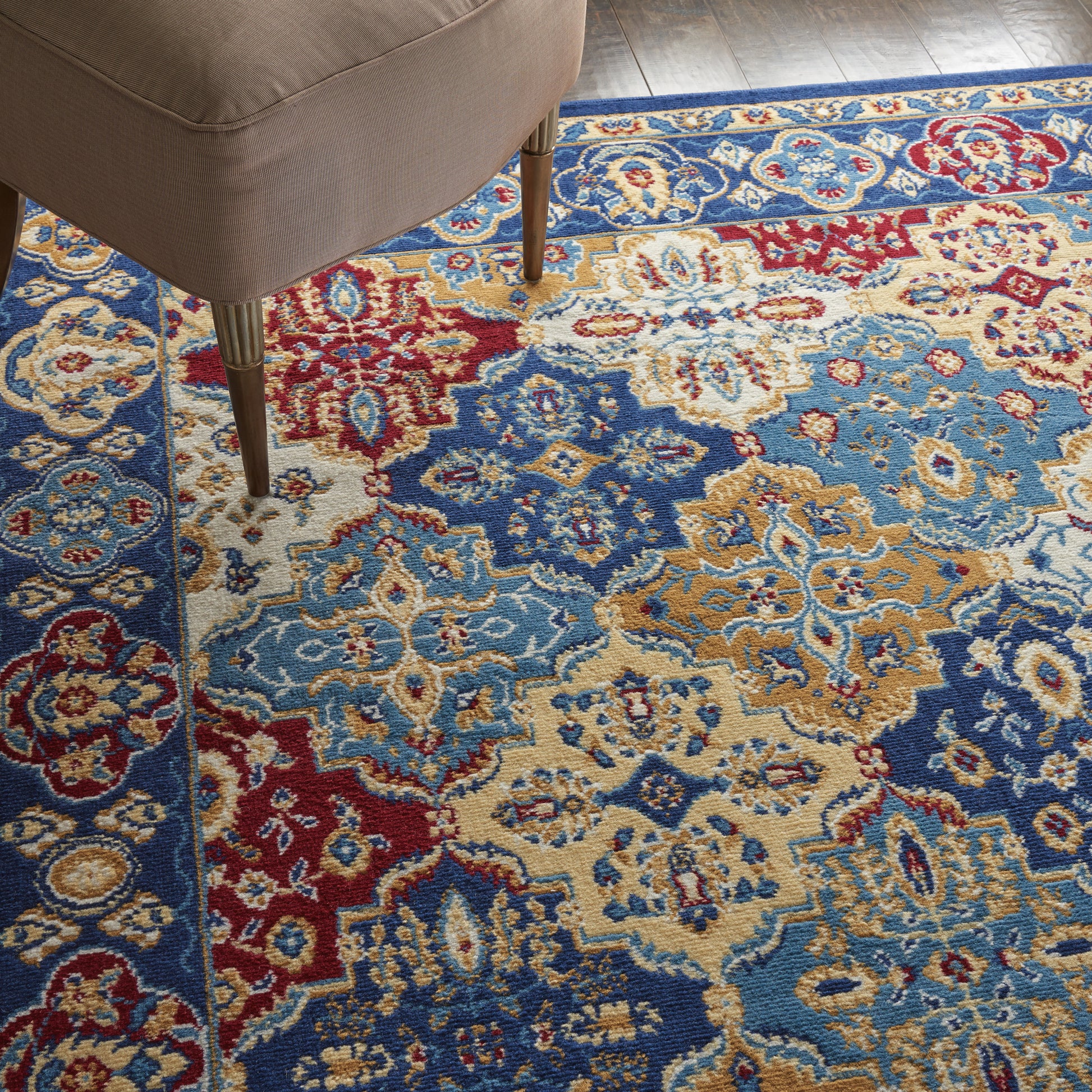Colorful Persian-style rug with blue, red, gold and cream floral patterns; beige chair leg visible.