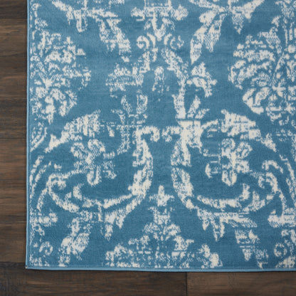 Blue & white damask-pattern rug on dark wood floor; ornate floral motif, rectangular area rug.
