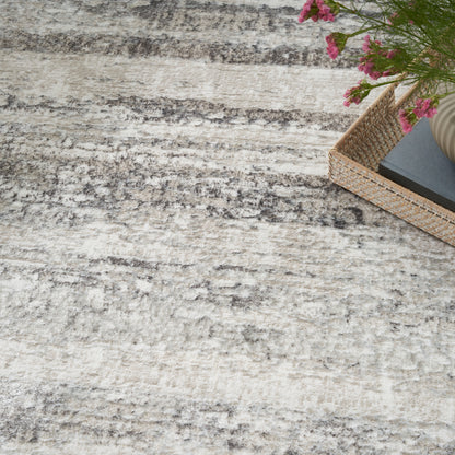 Light gray and cream textured rug with a woven basket containing a dark notebook and pink flowers in the corner.
