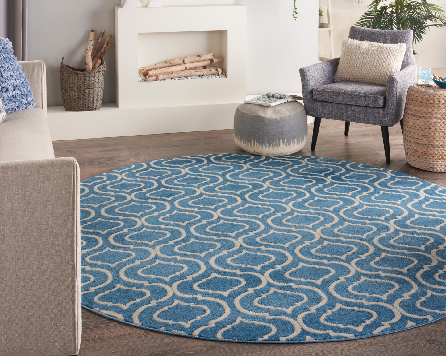 Round blue rug with white looping trellis pattern in a living room with gray sofa, armchair, and fireplace.