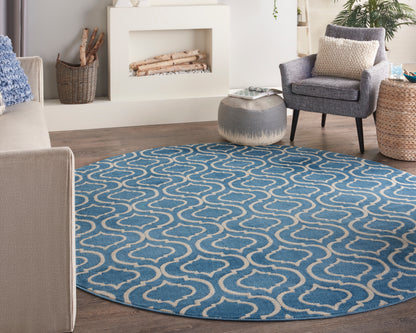 Round blue rug with white looping trellis pattern in a living room with gray sofa, armchair, and fireplace.