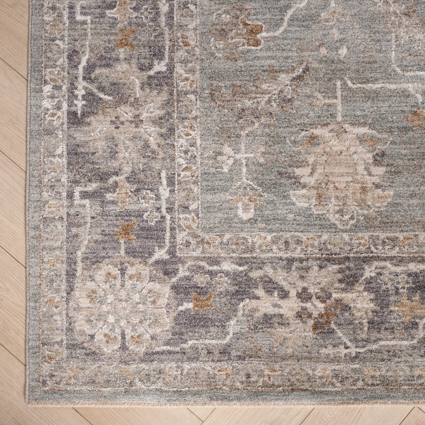 Persian-style area rug in muted blue-gray with ivory floral pattern and decorative border on a light wood floor.