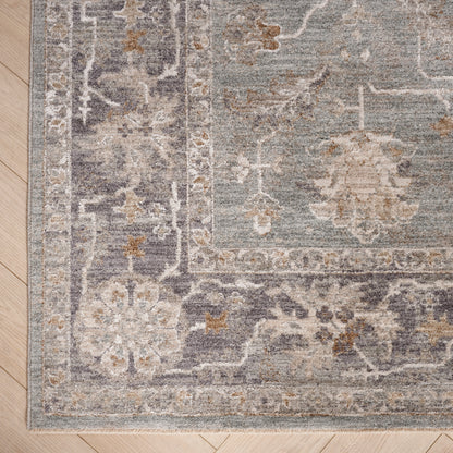 Persian-style area rug in muted blue-gray with ivory floral pattern and decorative border on a light wood floor.