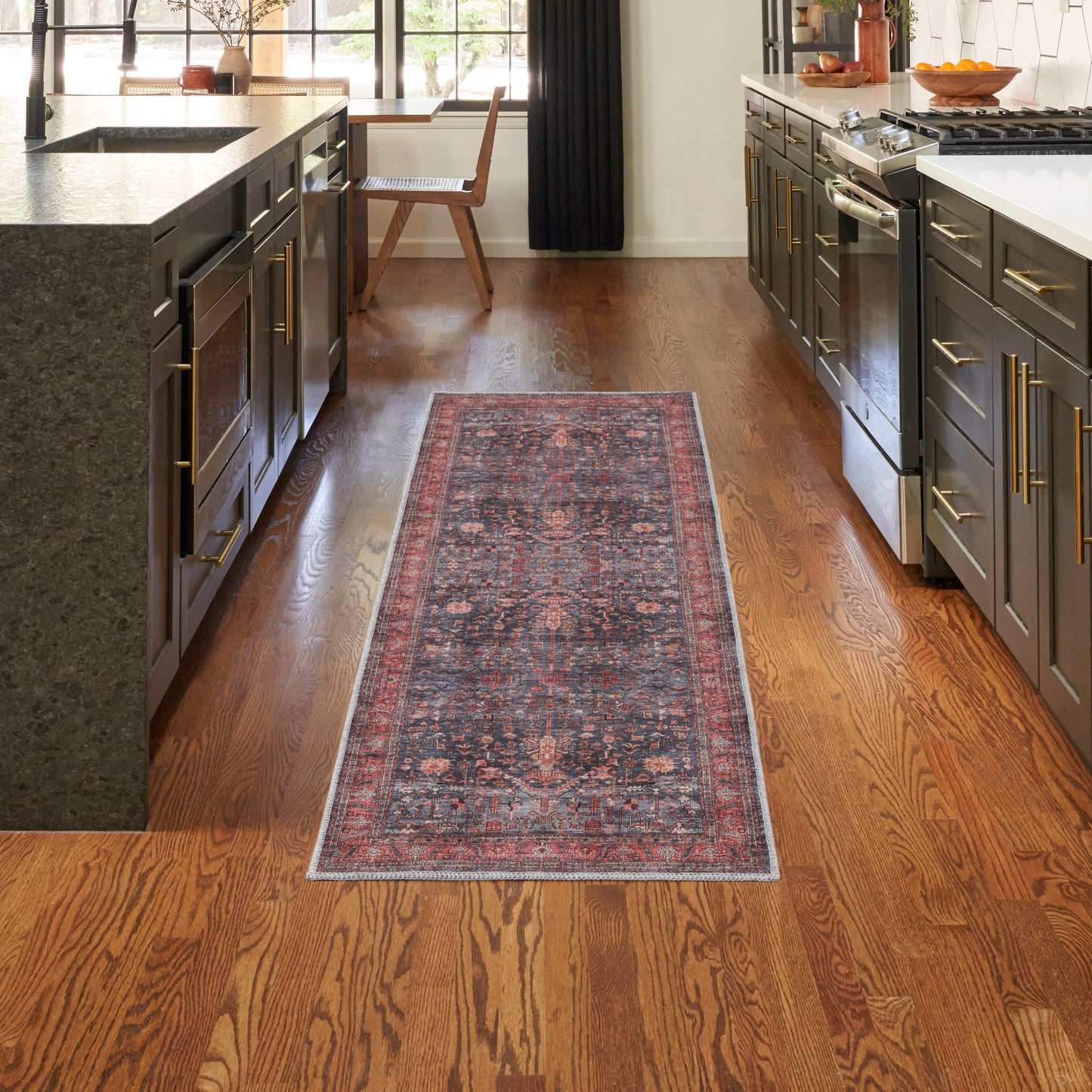 Long oriental runner rug with red and blue pattern between dark kitchen cabinets on a warm hardwood floor.