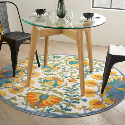 Round glass-top dining table with light wood legs, colorful floral rug, black metal chairs.