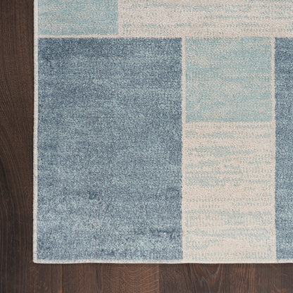 Blue geometric patterned area rug with block rectangles in dark blue, light blue & cream tones on dark wood floor.
