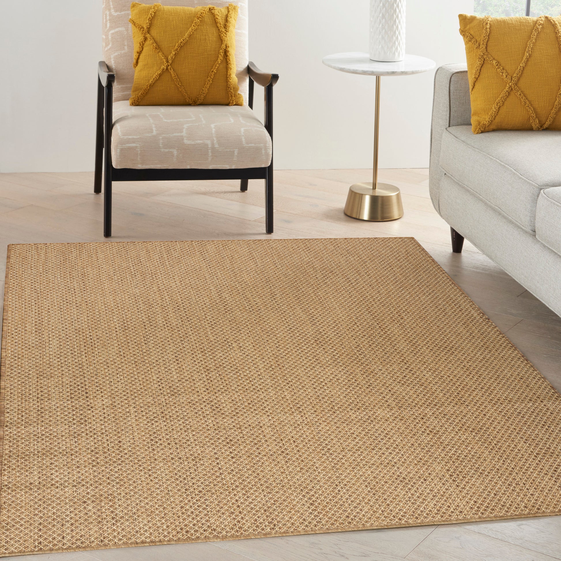 Natural jute area rug in a modern living room with mustard-yellow pillows, beige patterned armchair and a gray sofa.