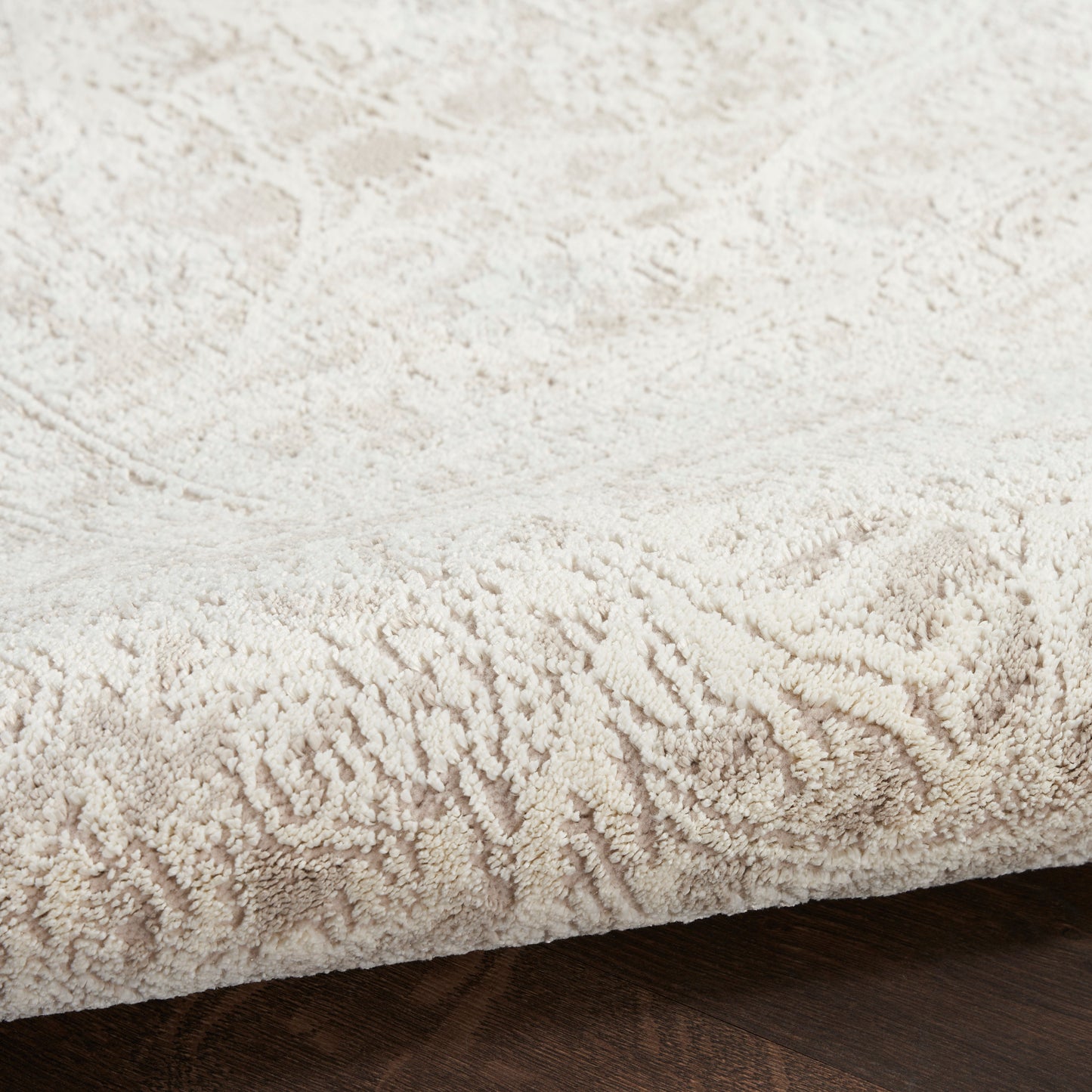 Cream plush area rug with a subtle damask pattern and a thick pile on dark wood floor.