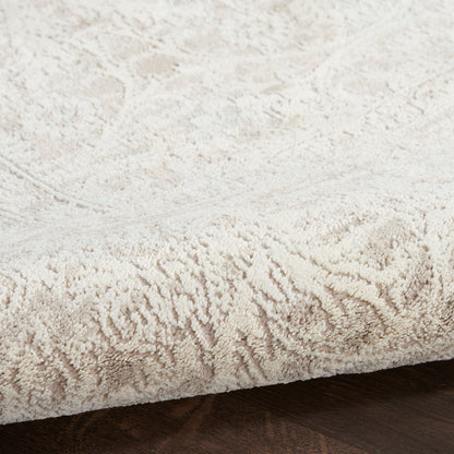 Cream plush area rug with a subtle damask pattern and a thick pile on dark wood floor.