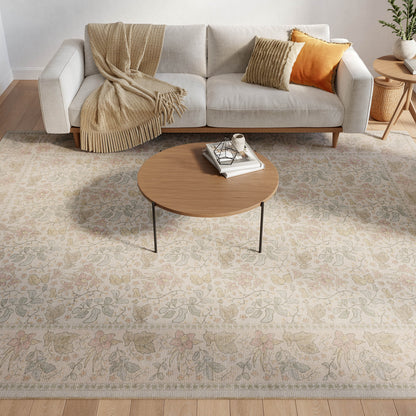 Cozy living room with a floral beige rug under a round wooden coffee table, light gray sofa, beige throw, and orange striped cushions.