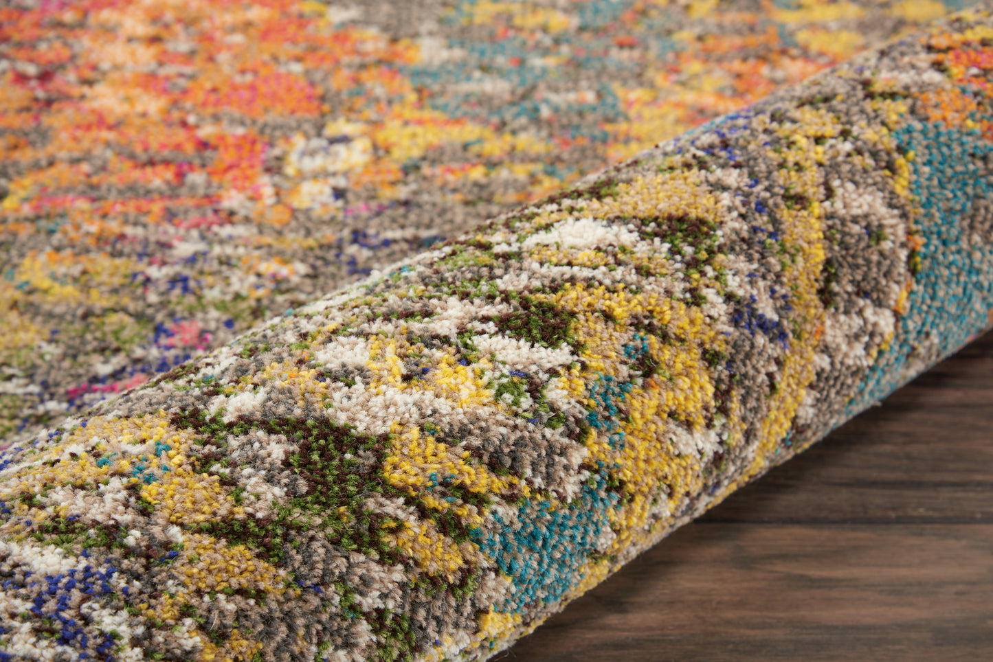 Rolled multicolor shag rug with vibrant mosaic-like pattern in yellow, blue, green and pink on a dark wood floor.