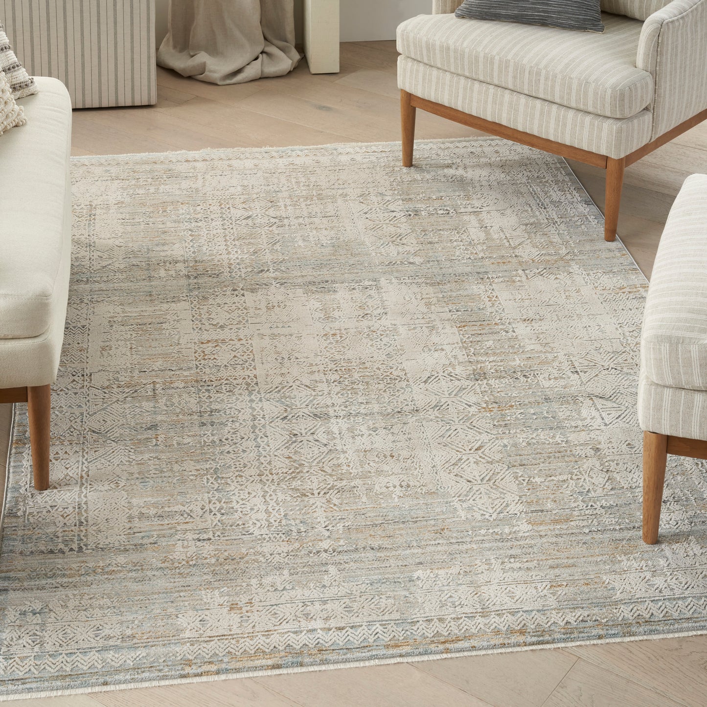 Neutral geometric patterned rug in beige, taupe and cream with cream upholstered chairs and light wood legs.