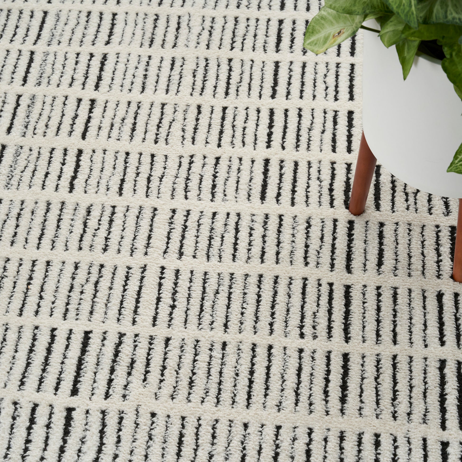Cream woven rectangular rug with black vertical dash stripes; modern floor decor for living spaces.