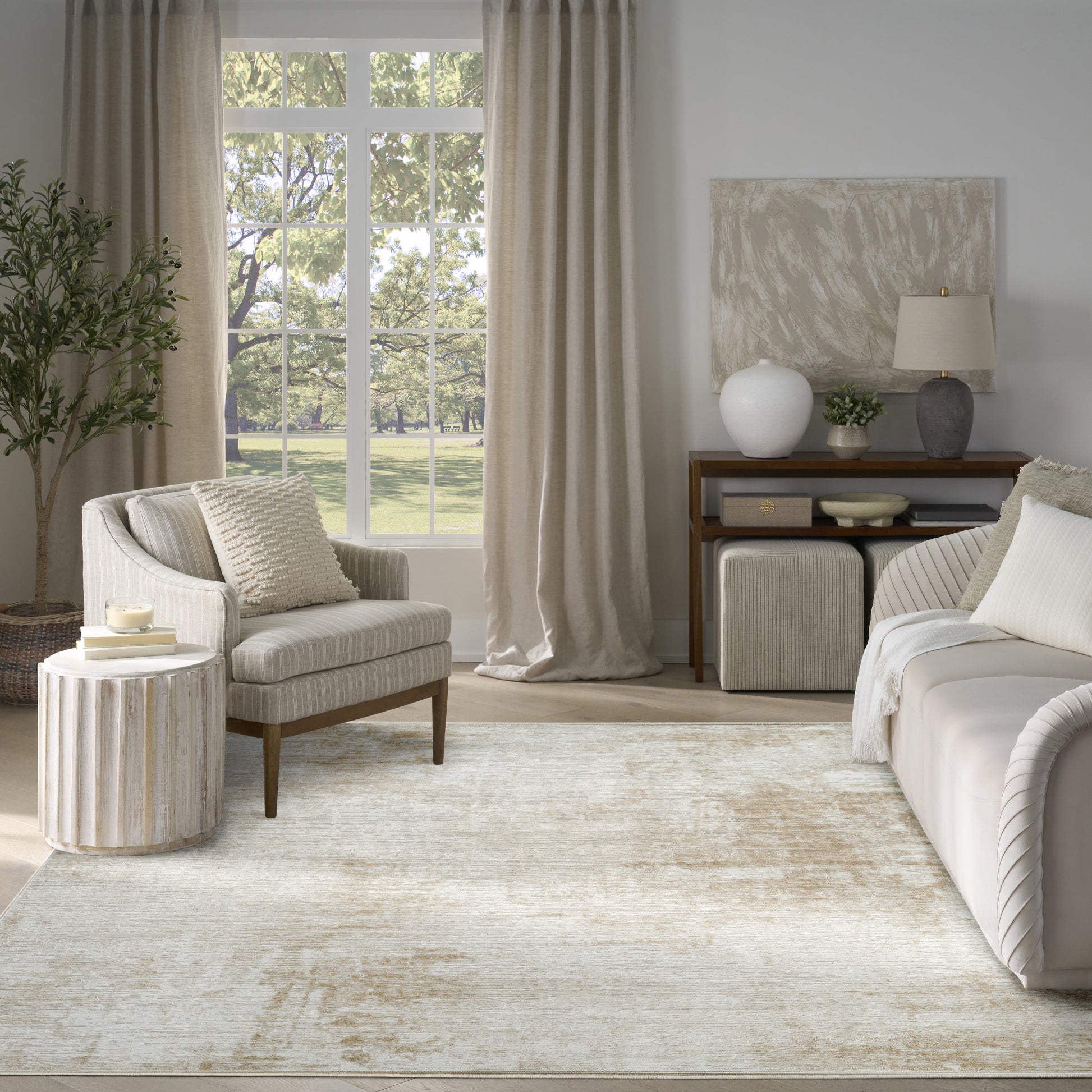 Neutral living room with cream sofa and armchair, beige curtains, textured rug, round side table, and console with vase.