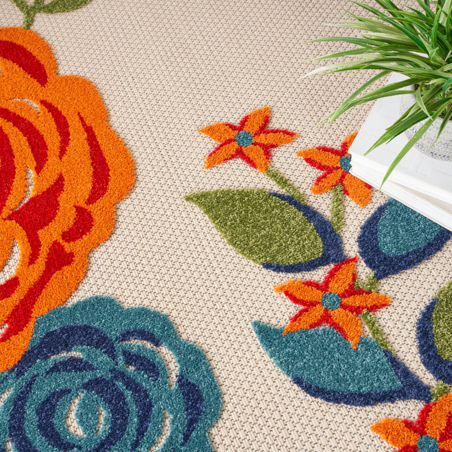 Beige textured floral rug with large orange, teal flowers & green leaves; white pot with green plant in corner.