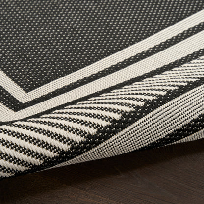 Close-up of black and white woven rug featuring bold geometric border, folded edge on dark wood floor.