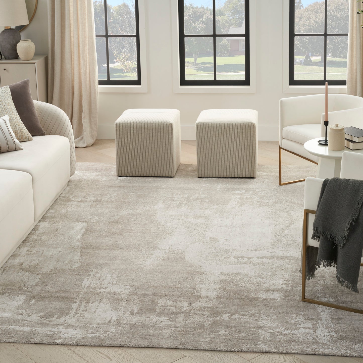 Bright contemporary living room with a beige rug, white sofa, beige ottomans, round coffee table, and black-framed windows.