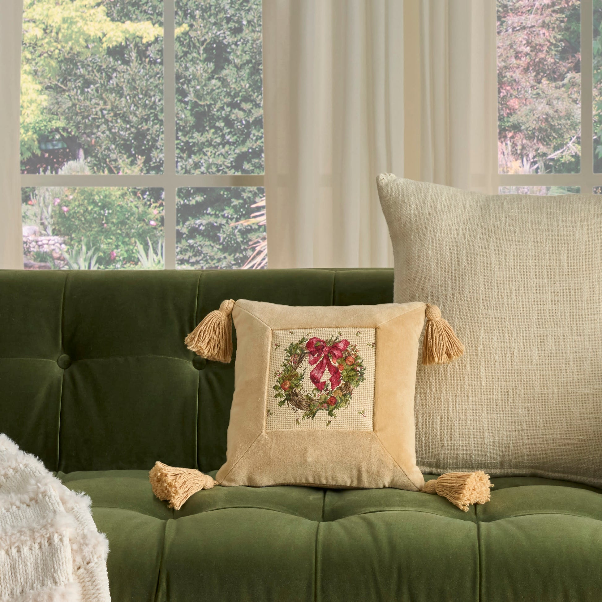 Olive green velvet tufted sofa with beige tasselled pillows; embroidered floral square cushion and beige lumbar pillow.