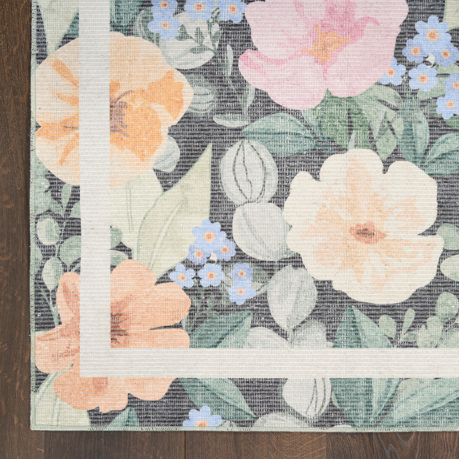 Floral woven rug with large peach and pink flowers, blue blossoms, green leaves, and white corner border on dark background.