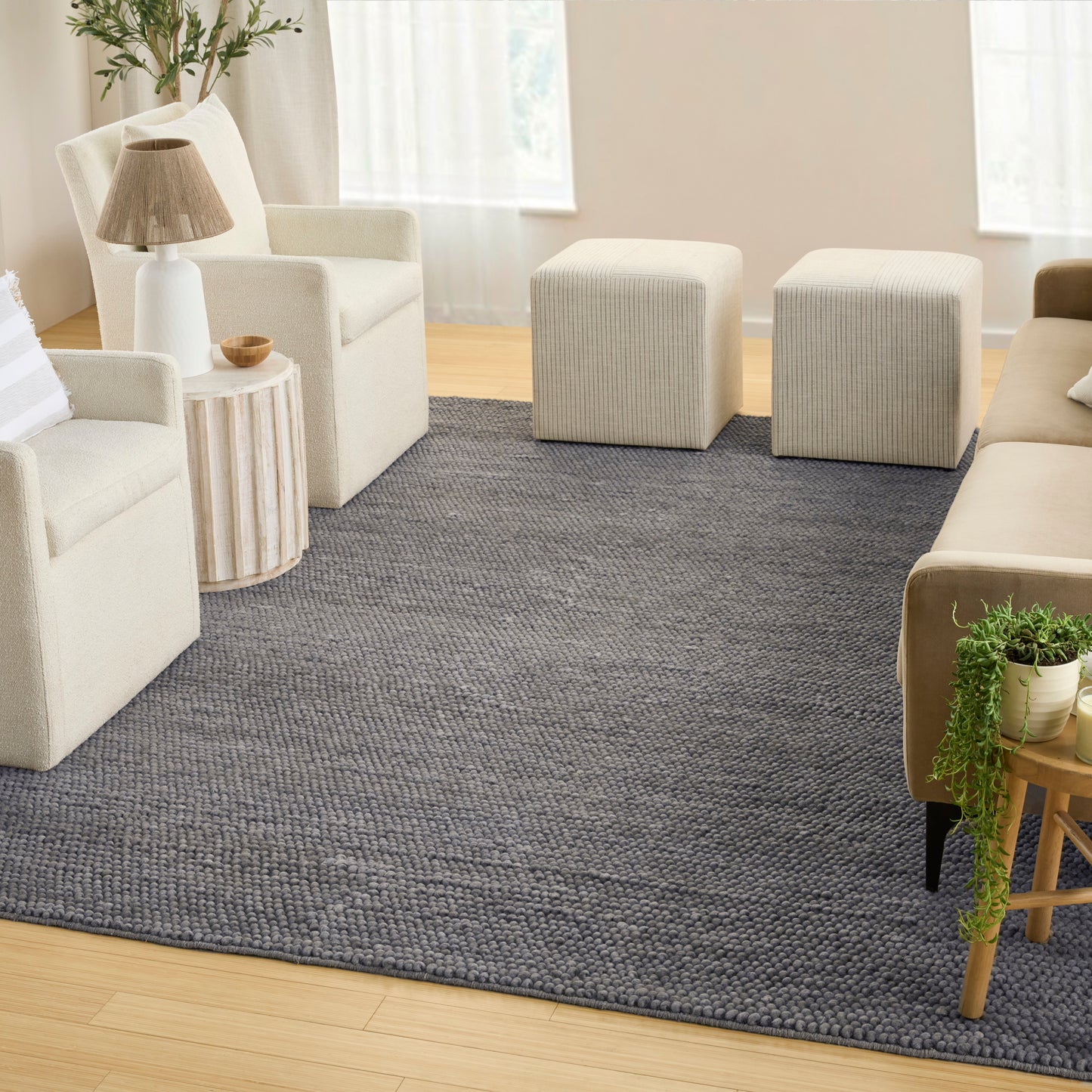 Neutral living room with cream fabric seating, grey boucle rug, two square ottomans, light wood side tables, lamp & plants