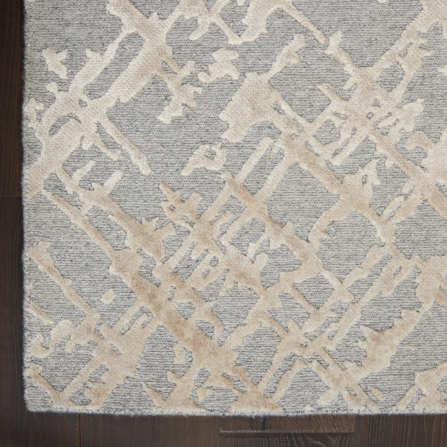 Gray rug featuring a cream abstract lattice motif and textured pile on dark wood floor.