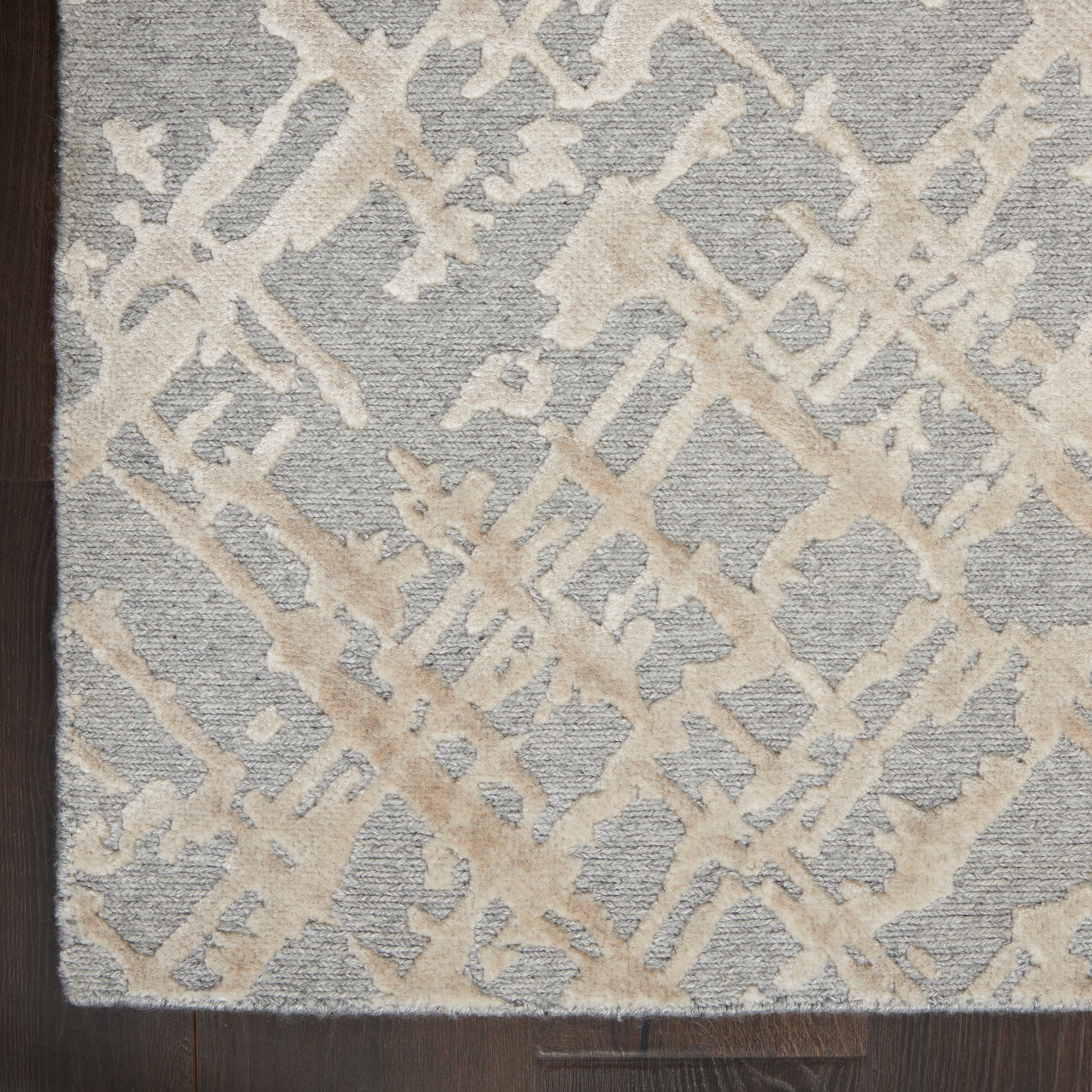 Gray rug featuring a cream abstract lattice motif and textured pile on dark wood floor.