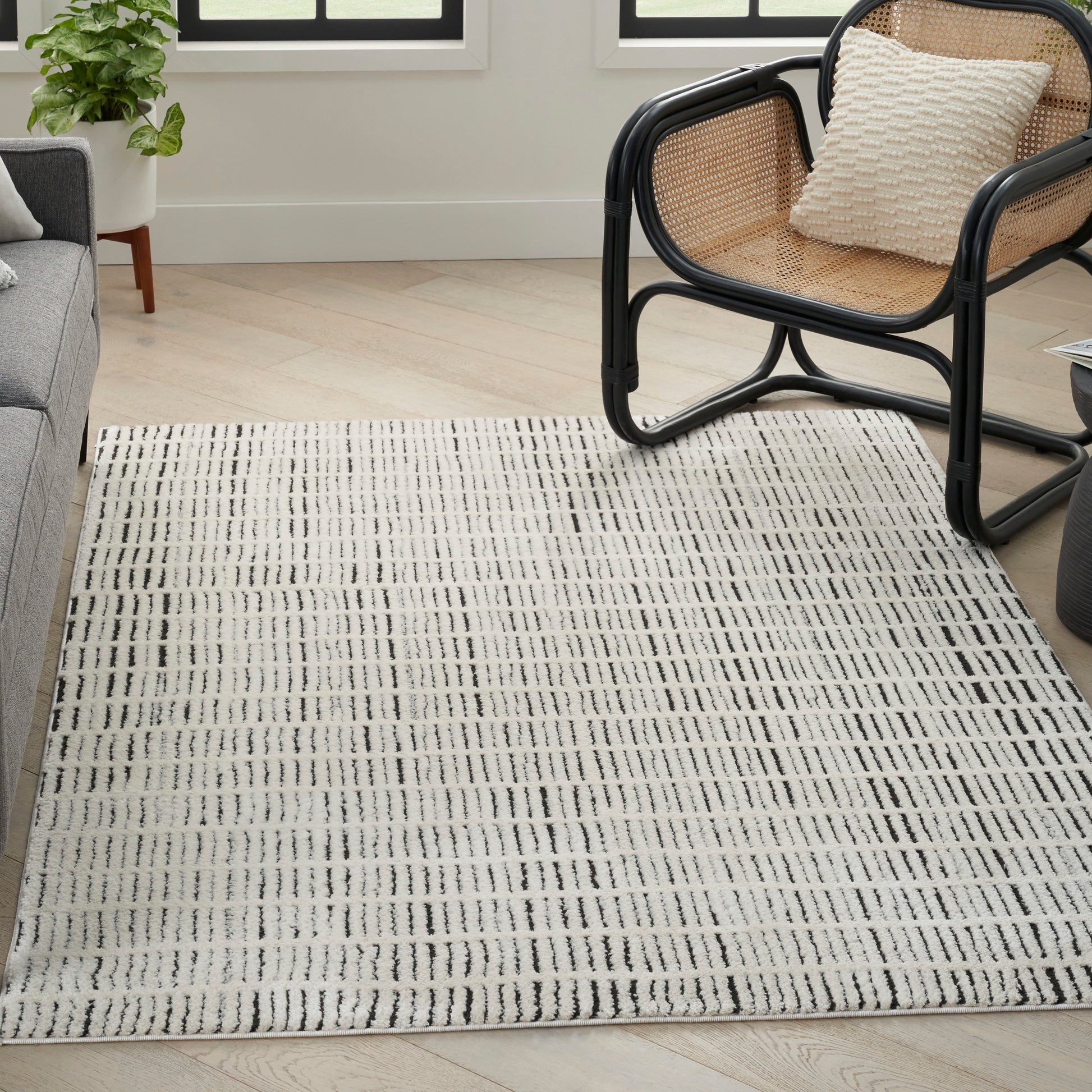 Rectangular flatweave rug in cream with a black linear grid; modern living room with a cane-framed chair.
