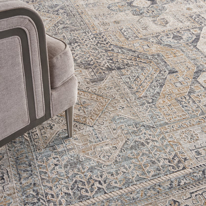 Grey-blue geometric area rug with intricate patterns; partial view of a plush grey armchair on the left.