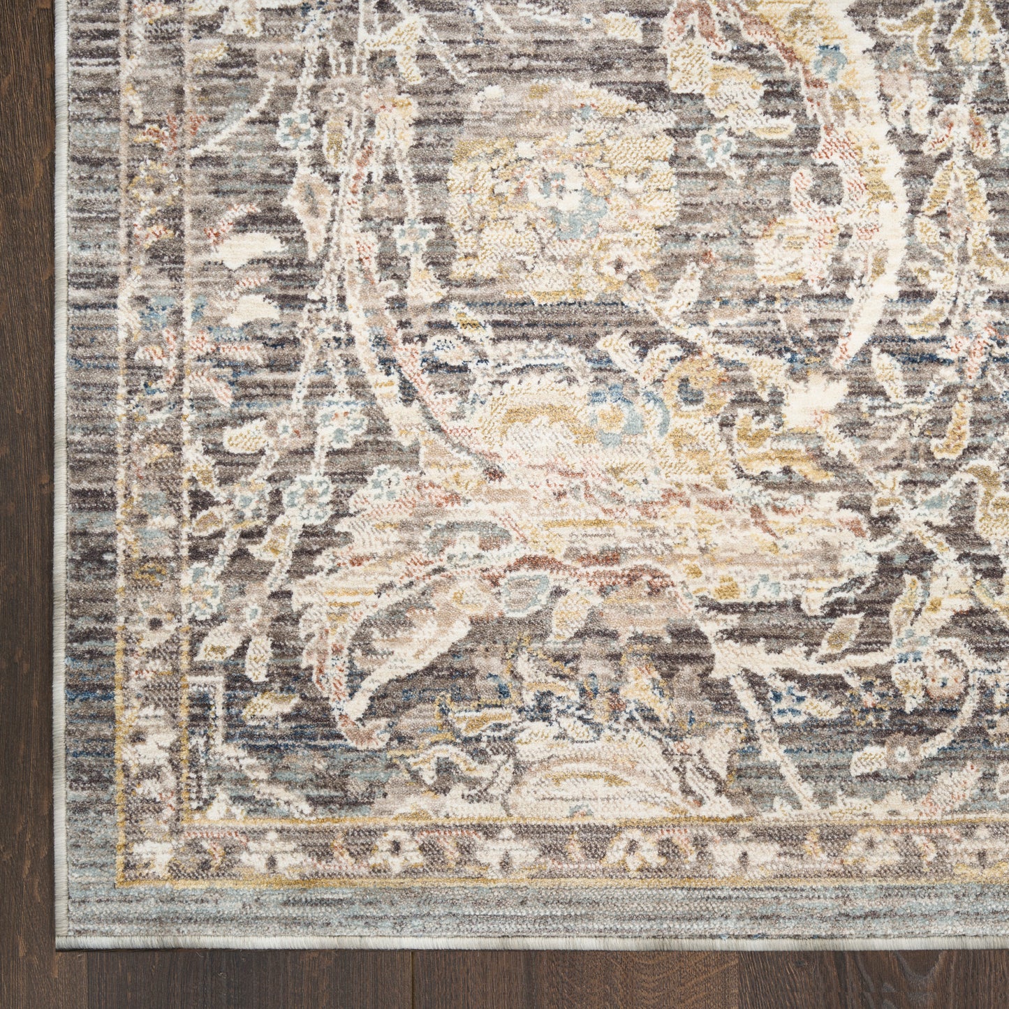 Grey-blue Persian-style ornate area rug corner with cream and gold floral motif on dark wood floor.